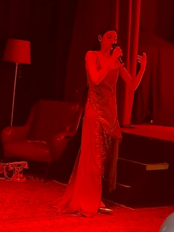 Tära al microfono sul palco, illuminata da luce rossa.