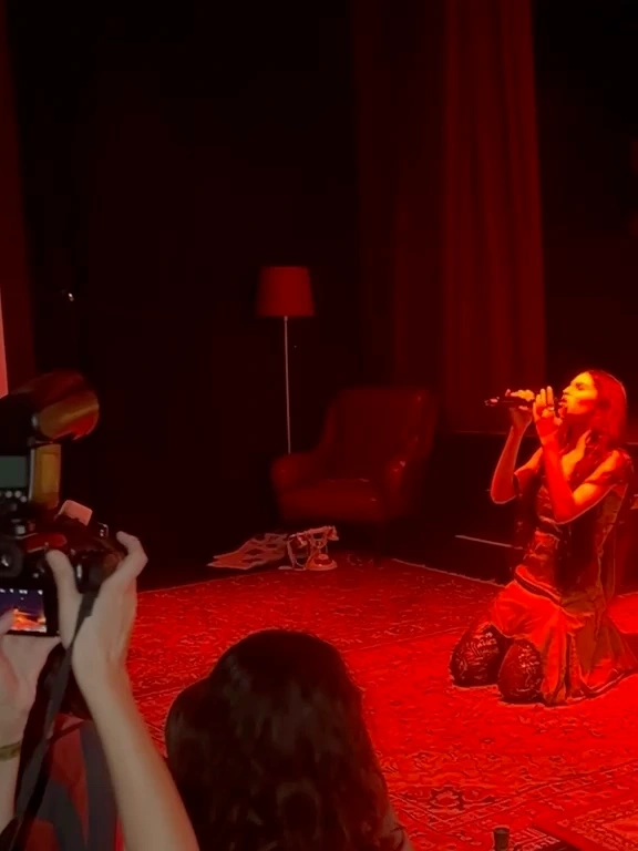 Tära canta inginocchiata sul palco sotto luce rossa.